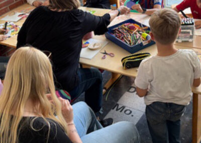 Die Kinder der Bastel-AG basteln gemeinsam an einem Tisch mit Papier, Stiften, Kleber und Scheren.