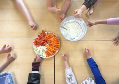 Auf dem Tisch steht eine Rohkostplatte und eine Schale mit Dip. Kinder strecken ihren Daumen aus und zeigen ihre Zustimmung.